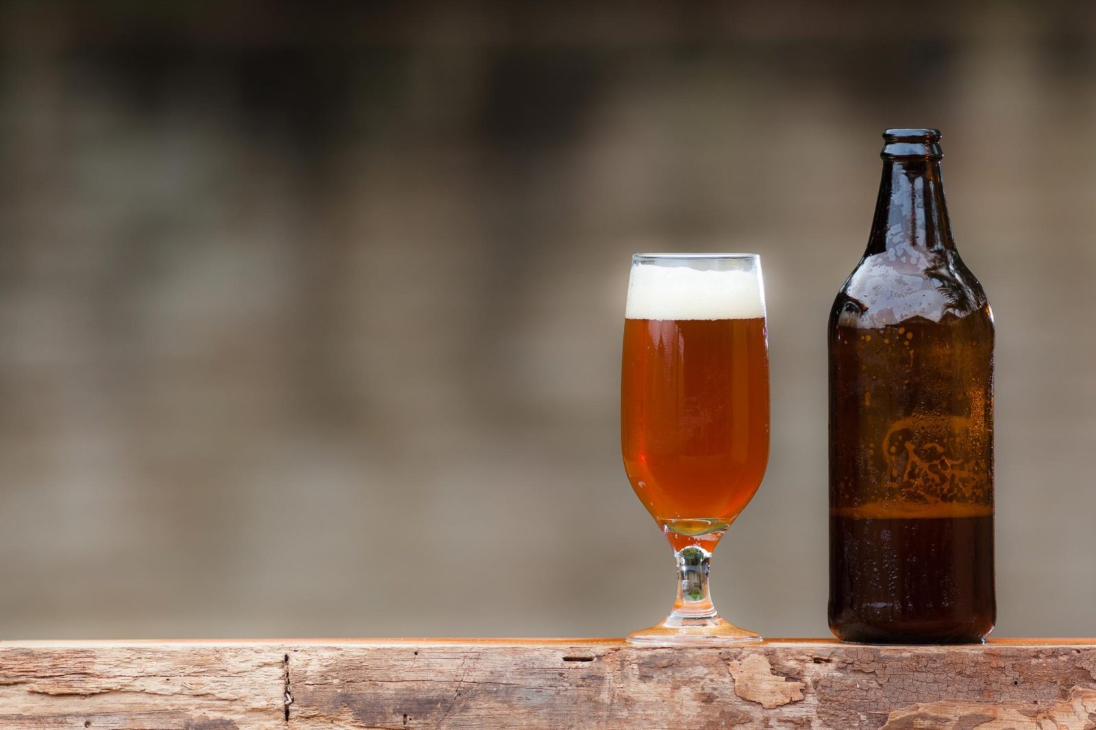 Bottle of homebrewed beer served outside on rustic table.